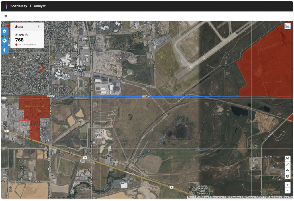 Screenshot of the SpatialKey Analyst web map showing a satellite view with a distance measurement line drawn horizontally across the map. The blue line represents a measured distance between two points, with the line extending across urban and rural areas. Red shaded polygons appear in parts of the map as reference layers. A stats panel on the left lists 768 shapes, indicating additional spatial data present during the measurement.