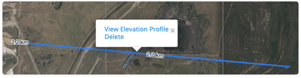 Map view showing a blue distance measurement line labeled 2.2 km drawn across the terrain. A pop‑up menu appears above the line with options to “View Elevation Profile” or “Delete,” indicating that the measured distance can be used to view elevation changes along the selected path.